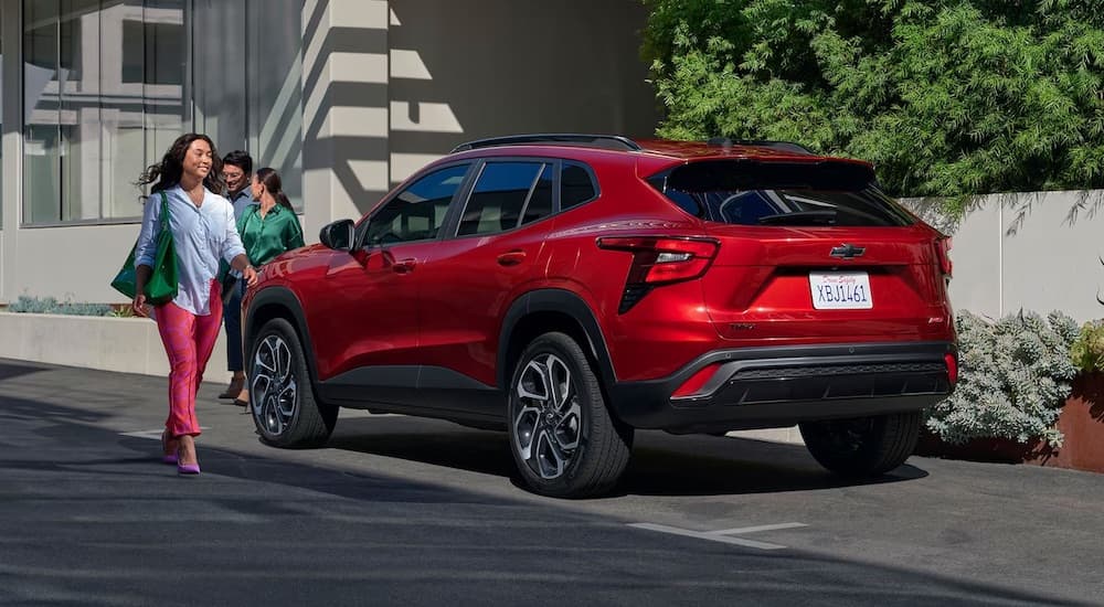 A person is shown walking from a red 2024 Chevy Trax is shown parked near a curb.