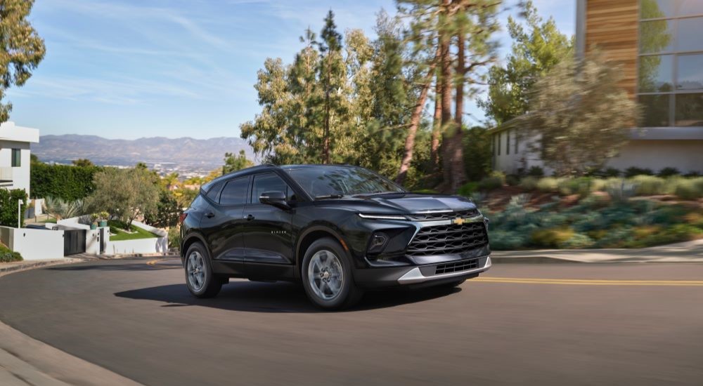 A black 2024 Chevy Blazer is shown driving through a suburb.