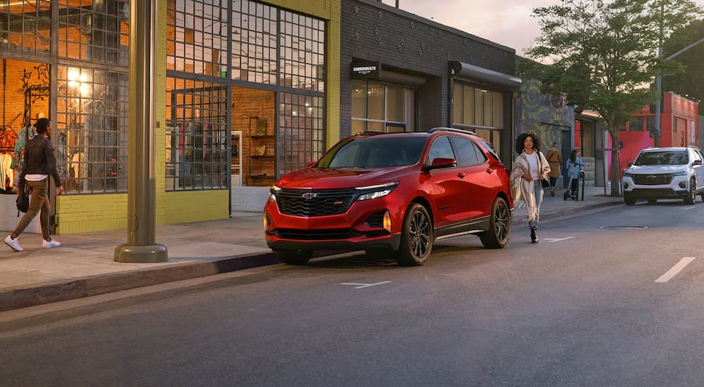 A red 2024 Chevy Equinox RS parked by a city curb.