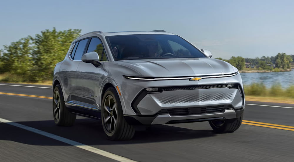 A silver 2025 Chevy Equinox EV driving down a road from a Chevy dealer near South Lyon.