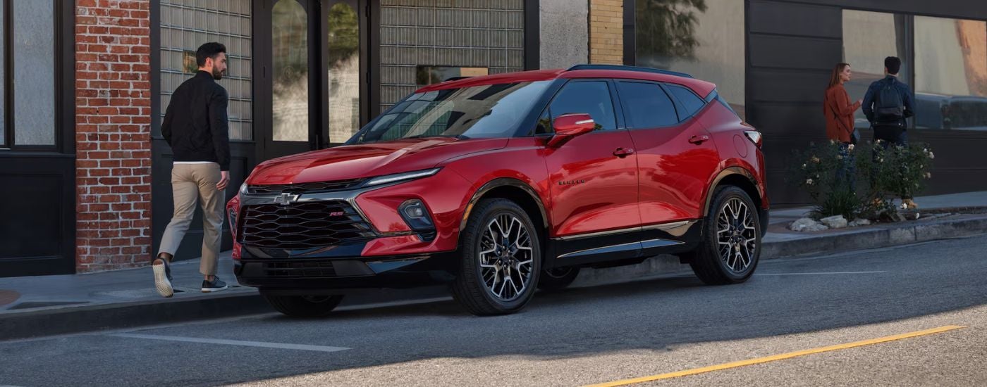 Red 2026 Chevy Blazer parked on a street in front of shops.