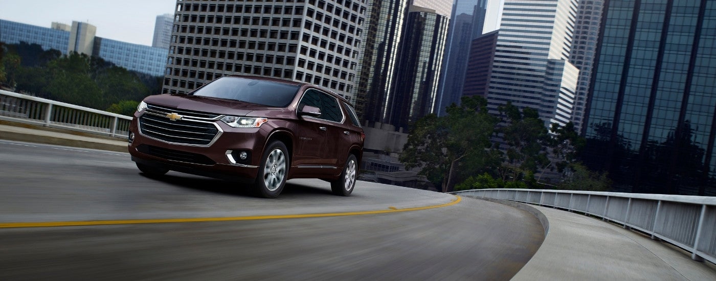 A maroon 2019 Chevy Traverse driving away from a city.