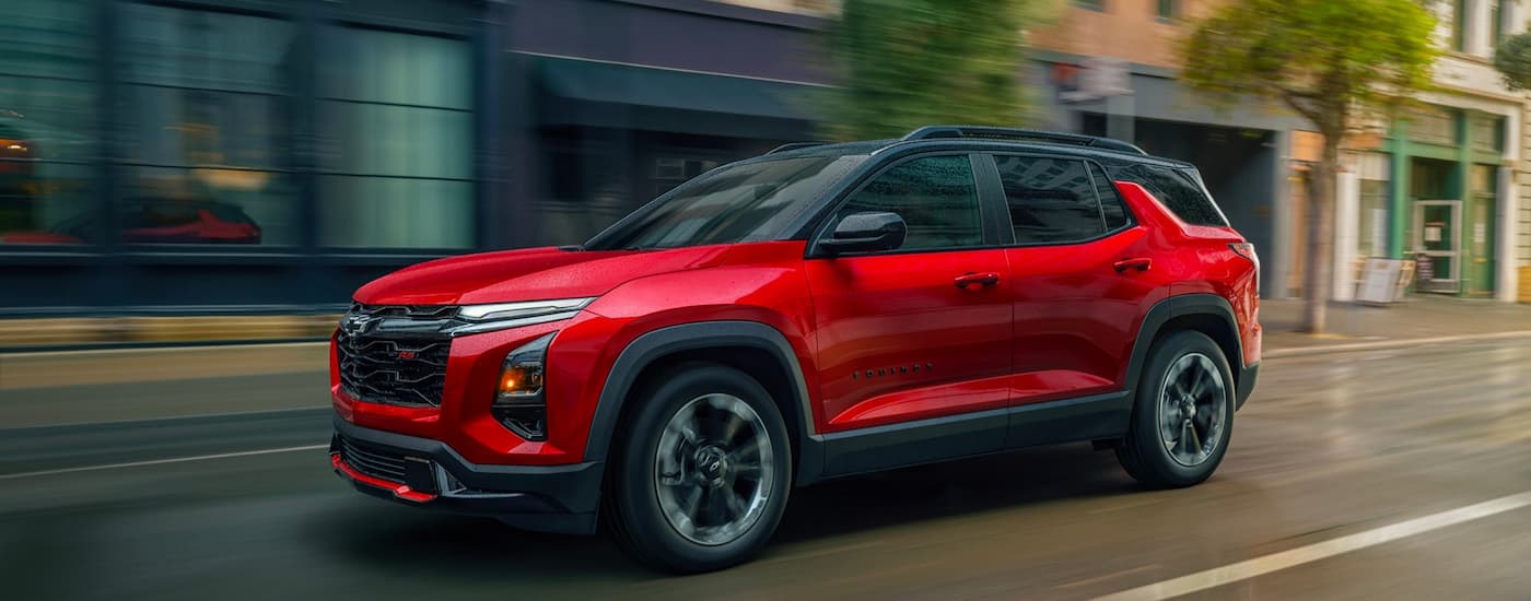 Red 2026 Chevy Equinox RS driving down a road from a car dealership in Plymouth.