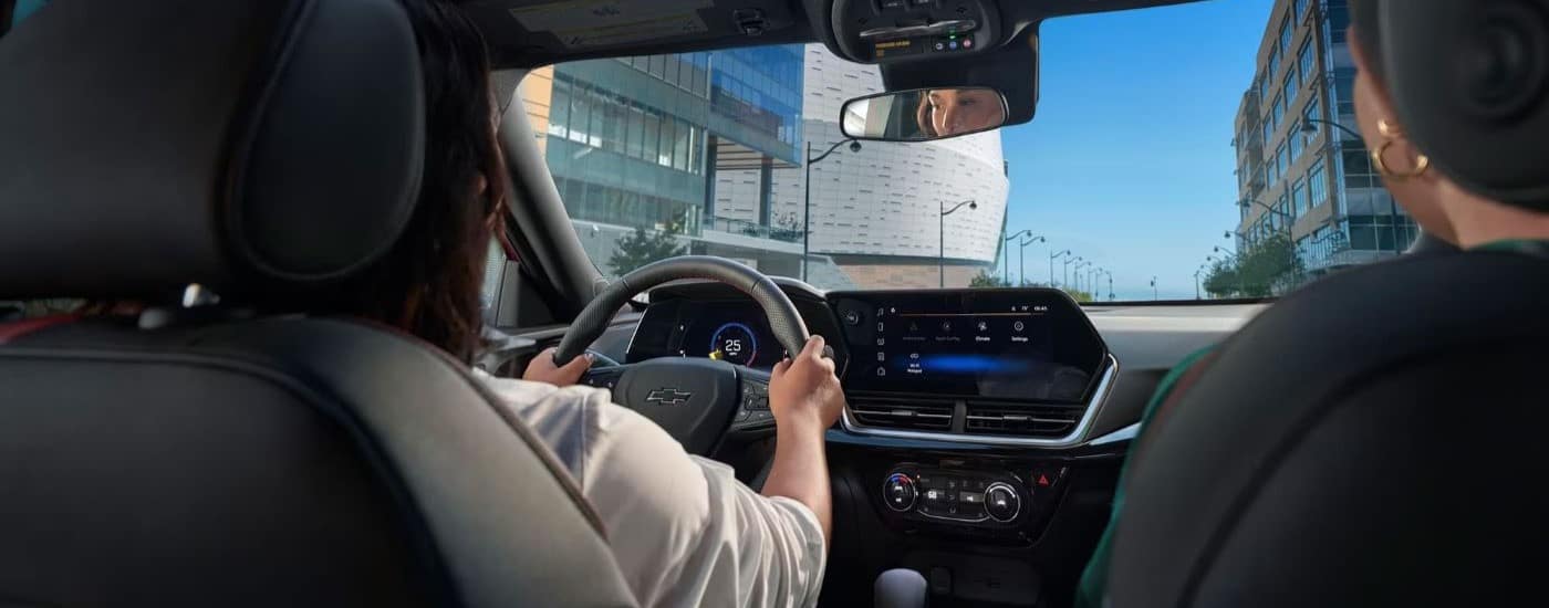 A person is shown driving a 2024 Chevy Trax on a city street.