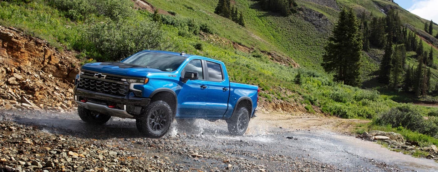 A blue 2024 Chevy Silverado 1500 ZR2 is shown off-roading through a creek.