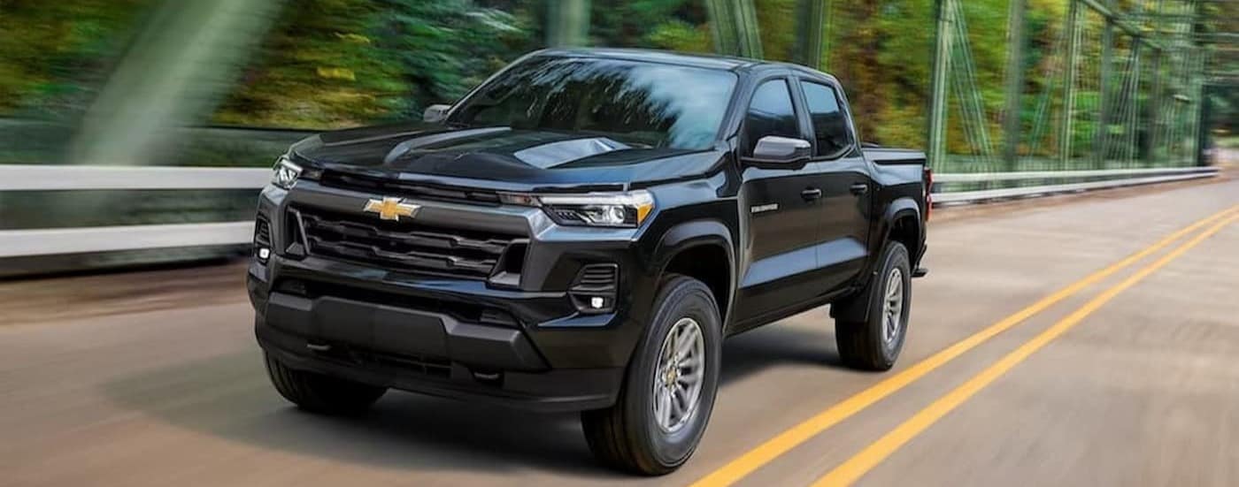 A black 2023 Chevy Colorado is shown driving on a bridge.