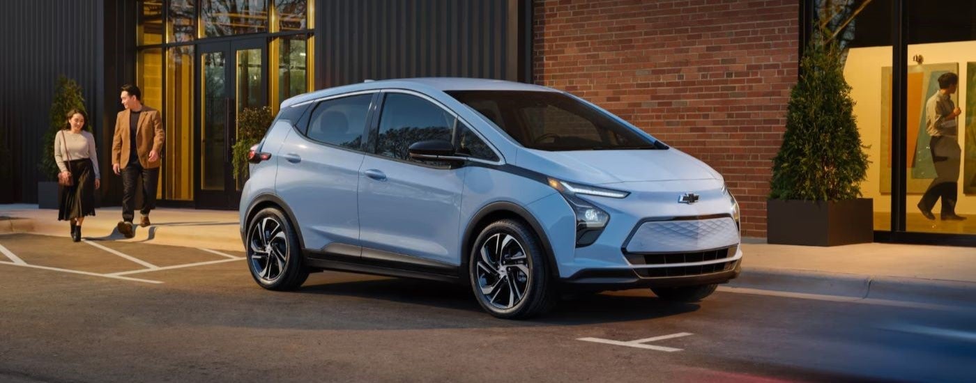 A light blue 2023 Chevy Bolt EV is shown in front of a brick building.