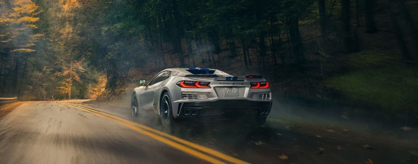 A silver 2024 Chevy Corvette E-Ray is shown from behind driving to a Chevy dealer in Plymouth.