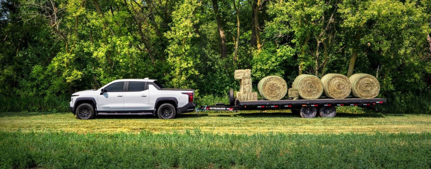 A white 2024 Chevy Silverado EV WT is shown towing large hay bales.