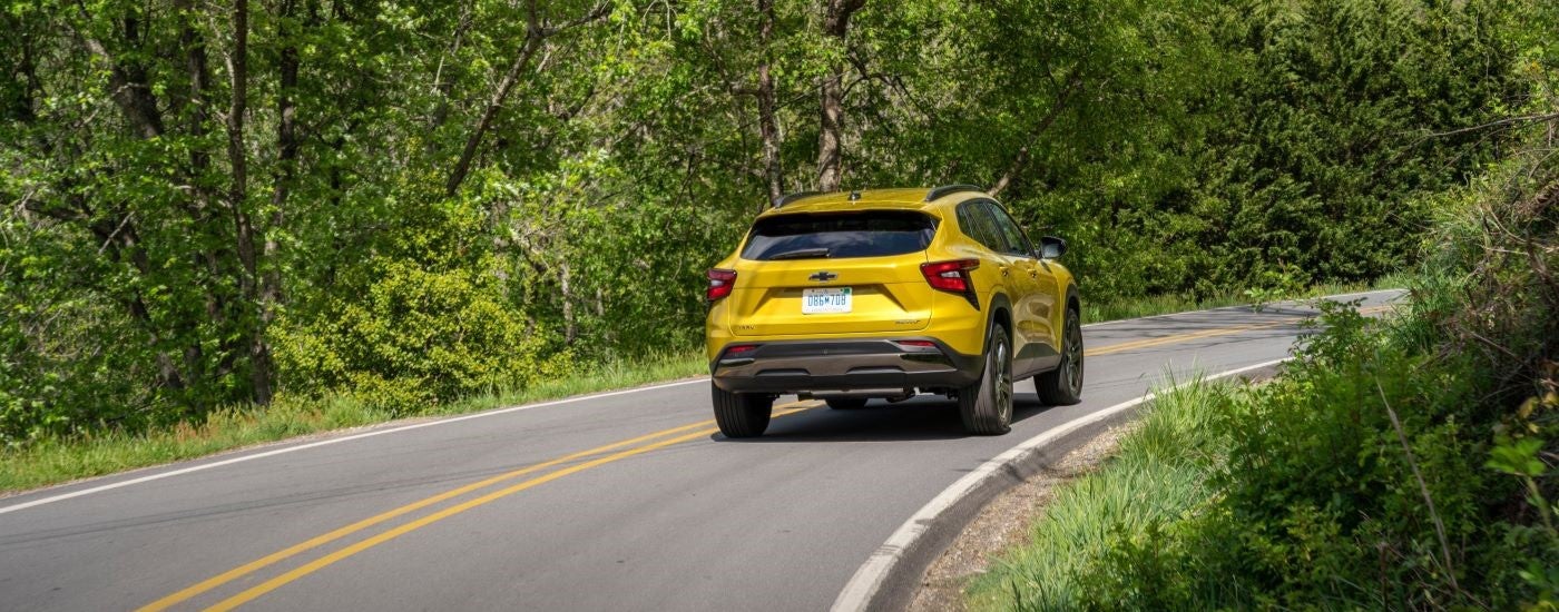 A yellow 2024 Chevy Trax Activ is shown from the rear driving on a tree-lined road.