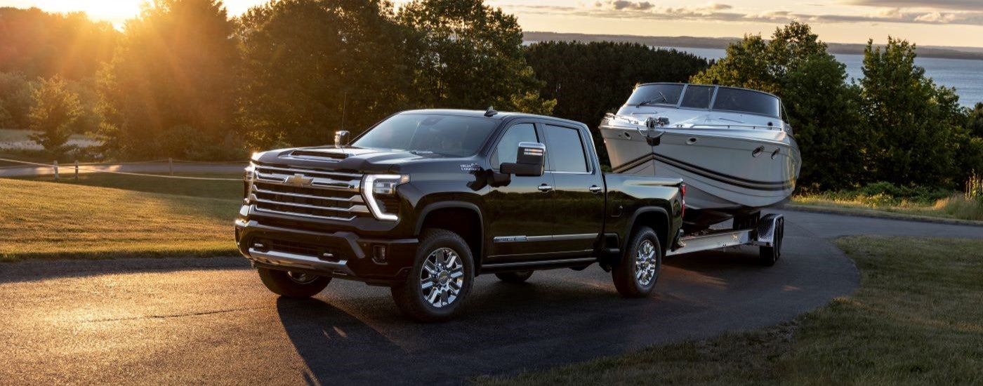 A black 2024 Chevy Silverado 2500HD High Country is shown towing a boat.