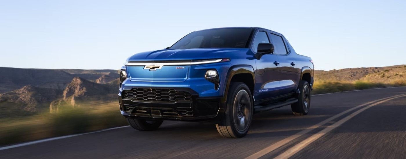 Blue 2024 Chevy Silverado EV RST driving from a dealer with EVs for sale.